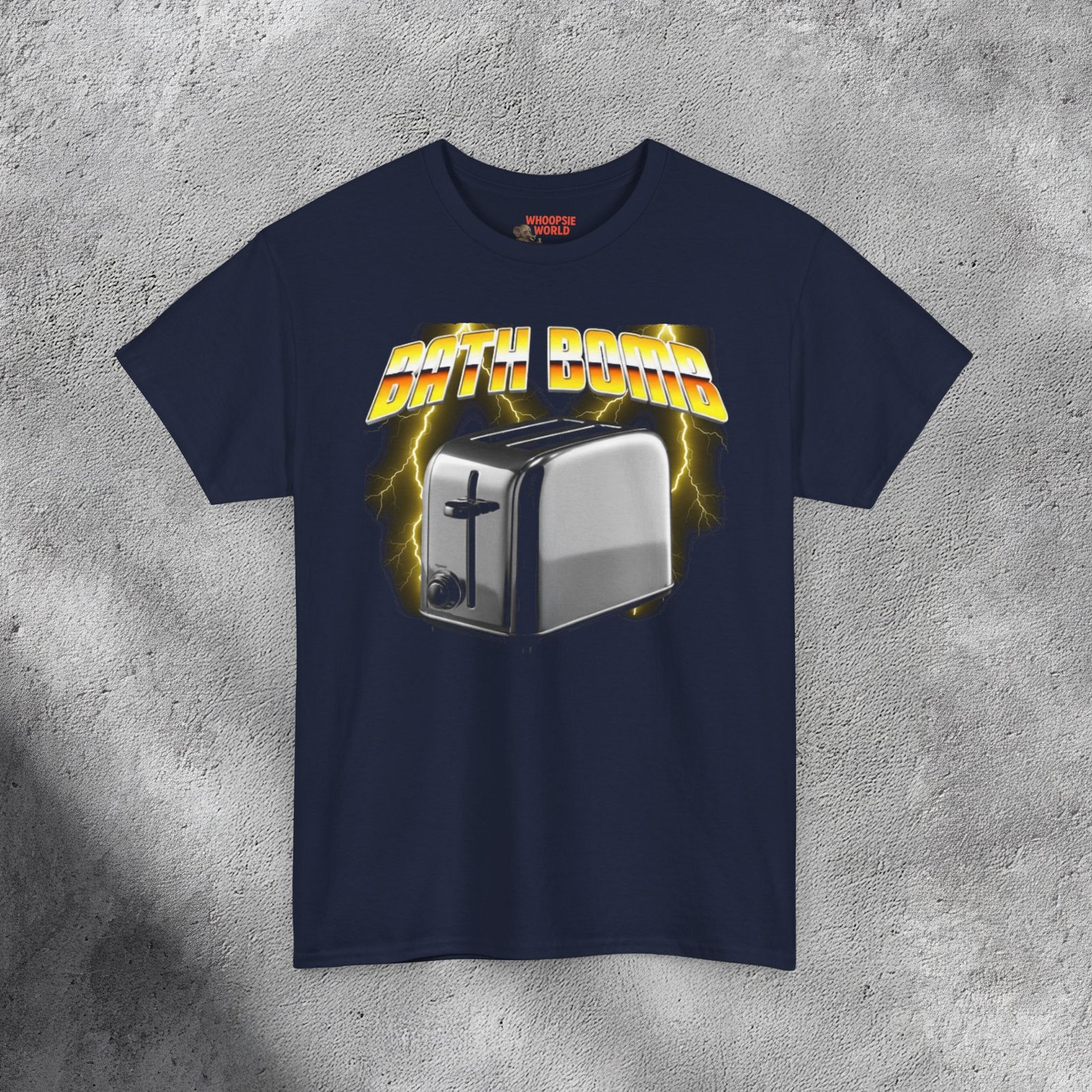The T-shirt features a bold and humorous design showing a shiny silver toaster placed in the center, rendered in a photorealistic metallic style. Behind it, vivid yellow lightning bolts illuminate a smoky dark background, giving the image an electrifying energy. Above the toaster, the words “BATH BOMB” appear in large 3D yellow-and-orange gradient letters with a chrome outline, styled like a retro 1980s power-metal logo. The mix of humor, danger, and vintage aesthetic gives the shirt a striking and edgy appearance.